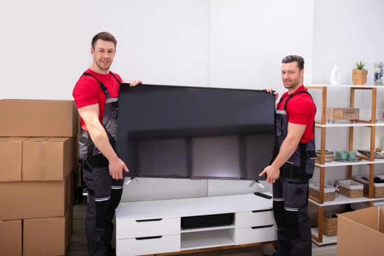 zwei männliche Profi-Umzugsunternehmen, die den Fernseher im Wohnzimmer transportieren